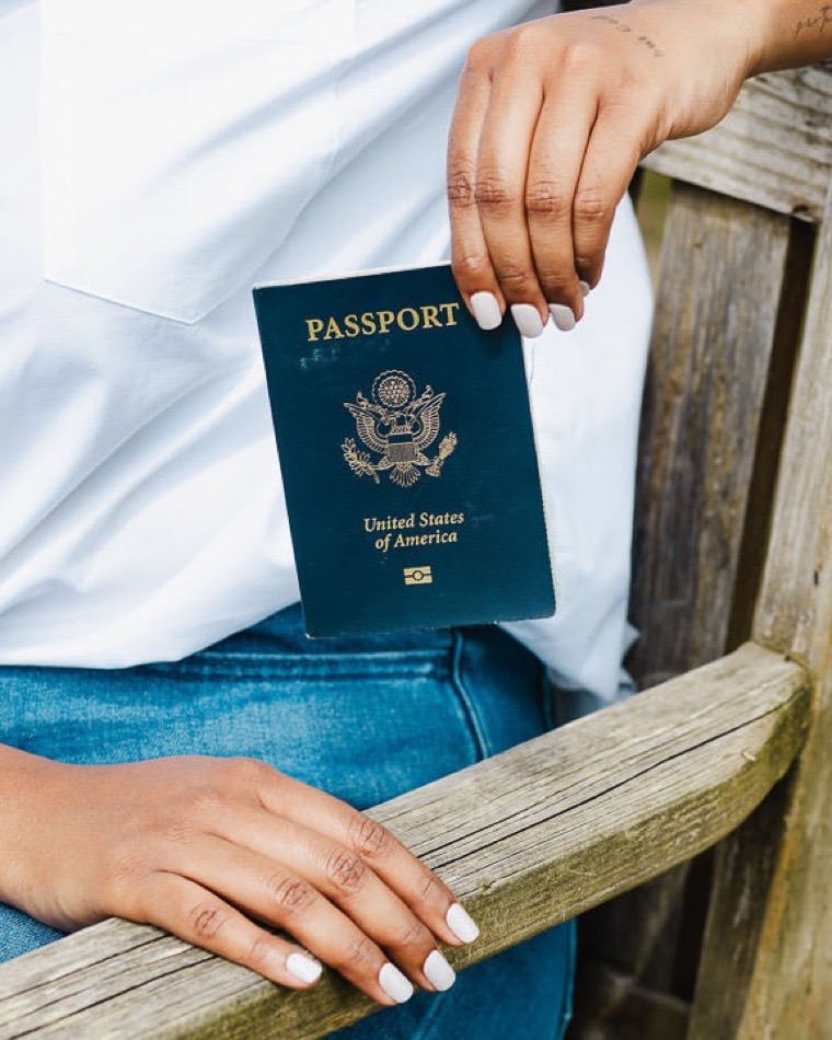 A close view of hands holding a United States passport against a weathered wooden fence rail, the status an extreme hardship waiver is filed to protect