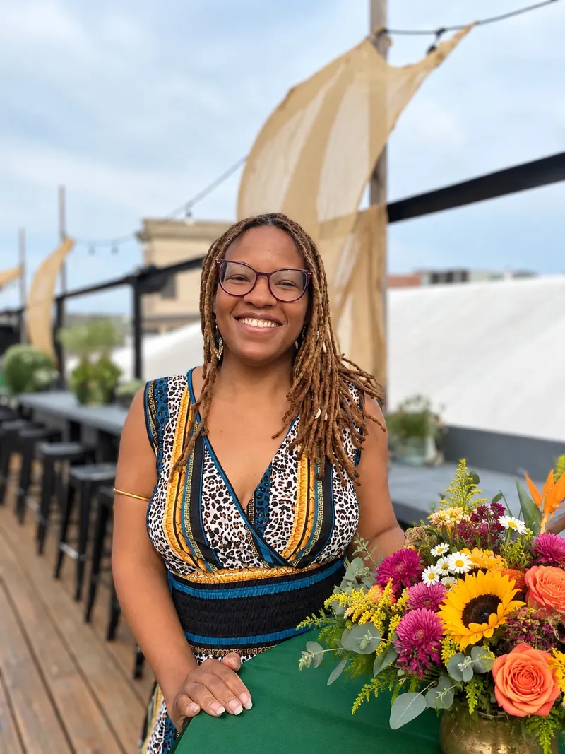 Jamila Kani, LICSW, EMDR and somatic trauma therapist at Life Migration Therapy, smiling on a rooftop beside a bouquet of flowers