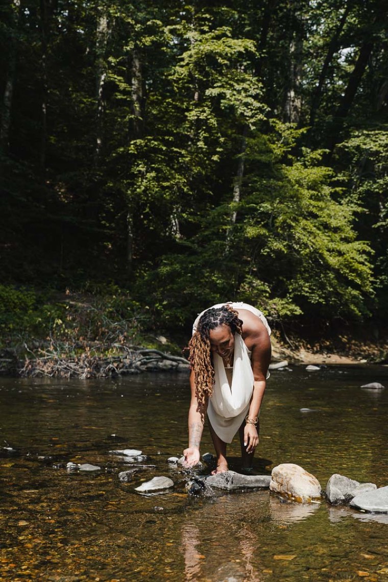 Charika White reaching into a forest creek in Maryland, the grounding work at the heart of trauma-responsive psychotherapy