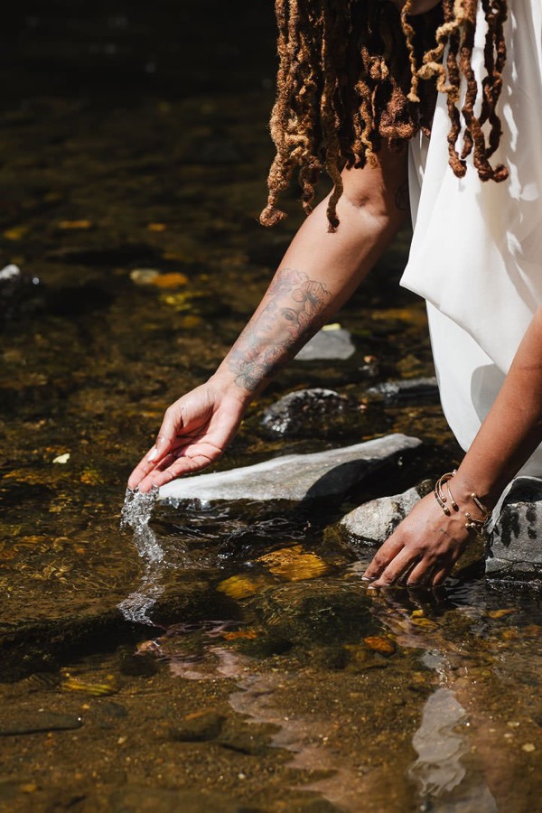Charika White's hands resting in creek water, the grounding and healing at the heart of Life Migration Therapy for DC and Maryland adults
