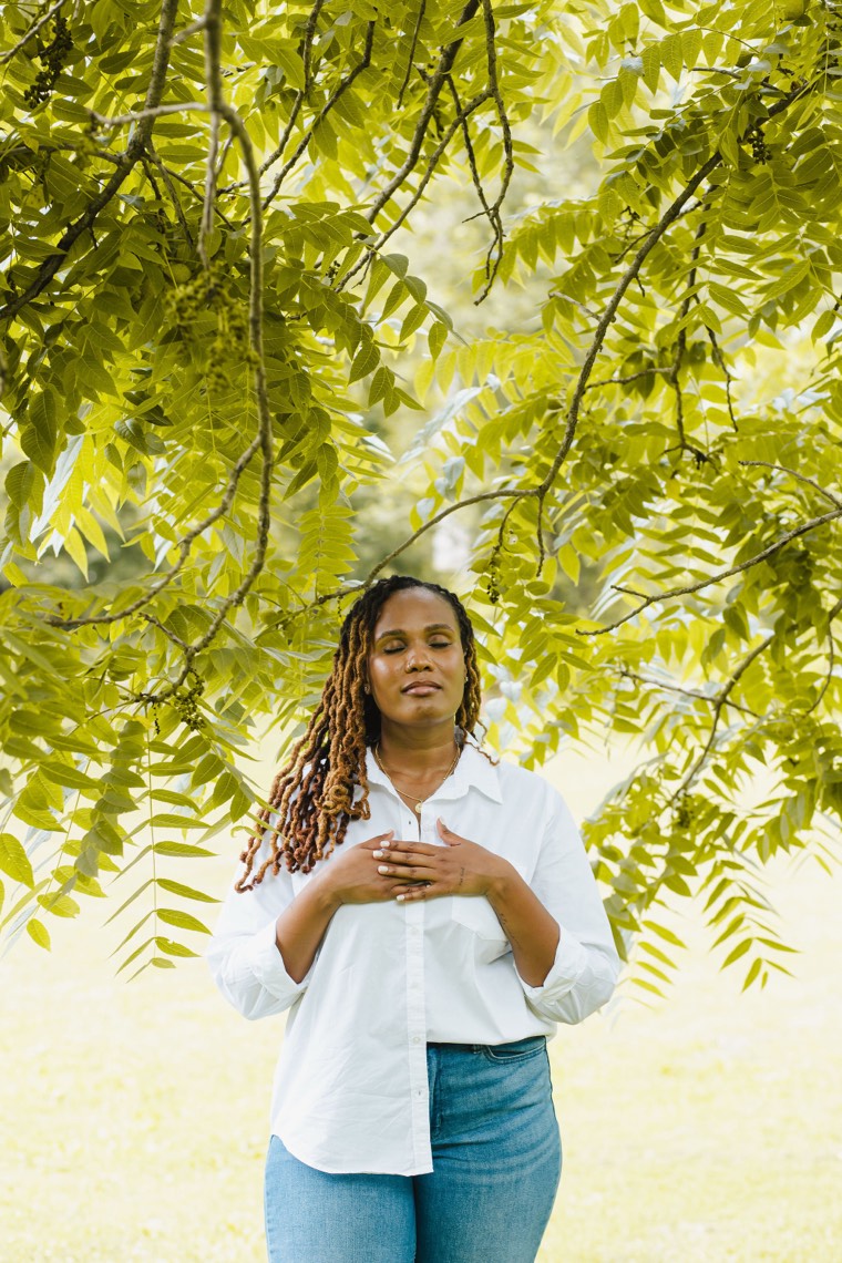 Charika White with her hands over her heart beneath walnut leaves, the confidential care inside every VAWA evaluation report for DC and Maryland survivors