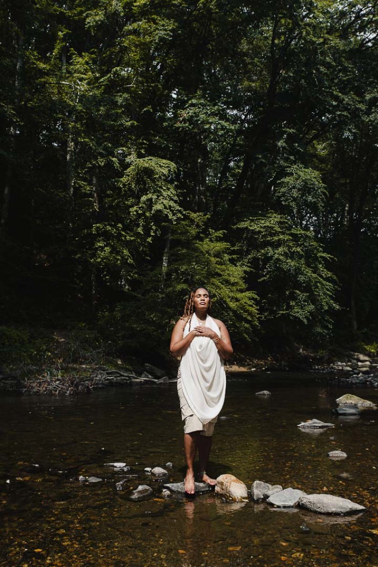 Charika White standing in a creek with her hand over her heart, the grounded care behind every VAWA psychological evaluation in Washington DC
